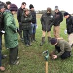 A group of people standing in a field discussing soil structure at the Girrick Farm Soil & Nutrient Network farm meeting