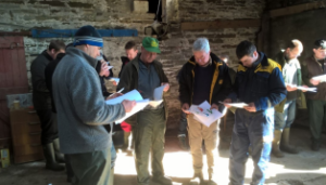 A group of farmers at the Knockglass Soil & Nutrient Network Farm, standing in a circle and reading through some papers giving a background to the farm
