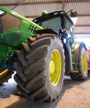 a photo of the front of a John Deere tractor taken from ground level with the primary focus on the front tyre