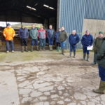 A group of farmers standing with their backs to a cattle shed in a farm yard.