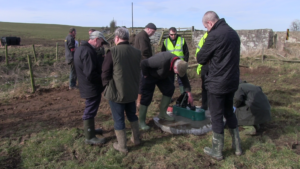 A group of farmers looking at and discussing a pasture pump in situ in a pasture field