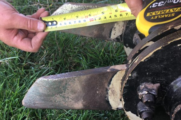 A photo of someone measuring the length of blade on a soil aerator with a yellow measuring tape