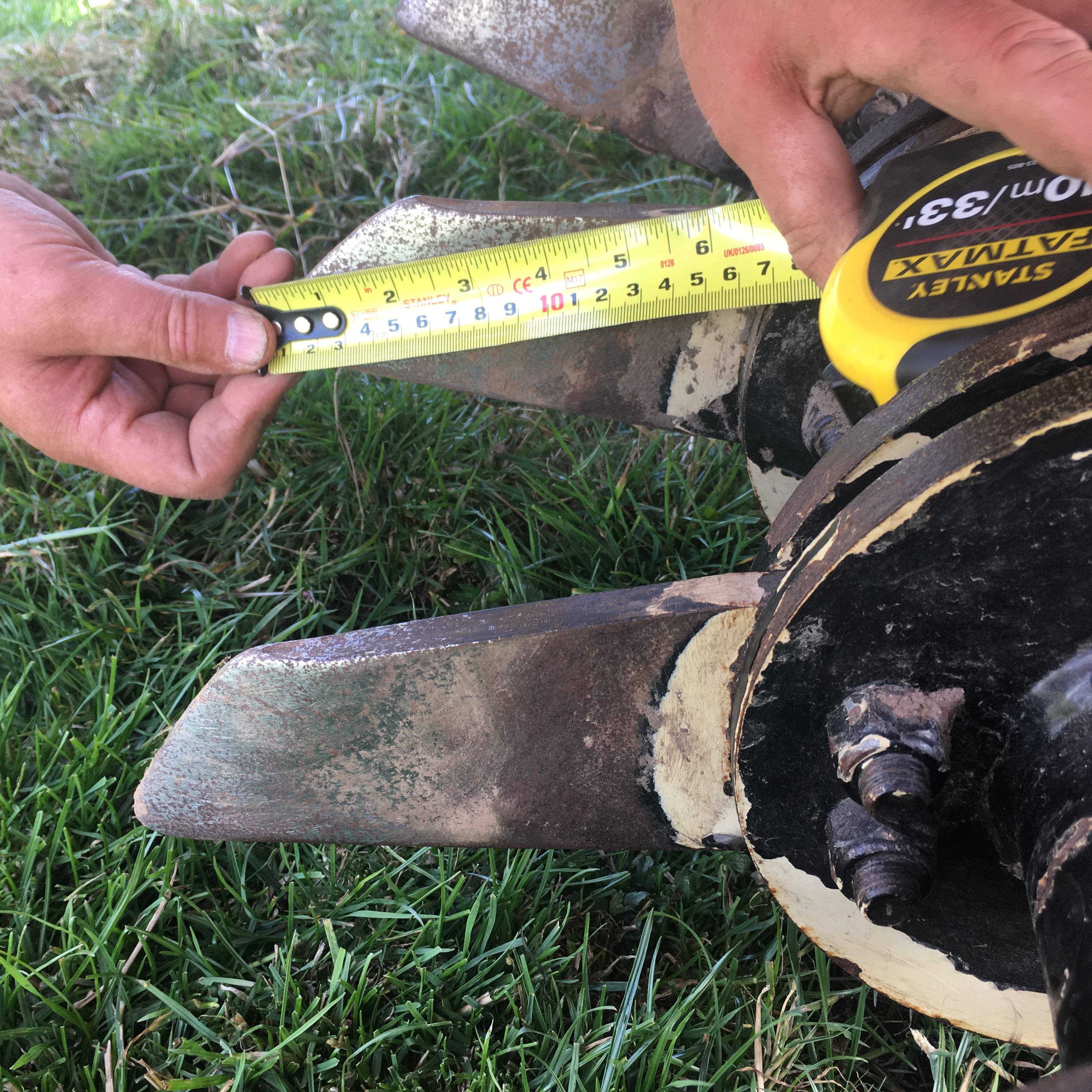 A photo of someone measuring the length of blade on a soil aerator with a yellow measuring tape
