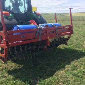 An aerator attached to the back of a John Deere tractor