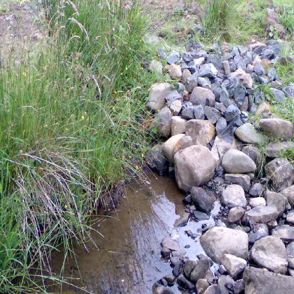 A water extraction point in a watercourse. There are a lot of river stones that can be seen from which the watercourse appears from. The abstraction point is below the river stones.