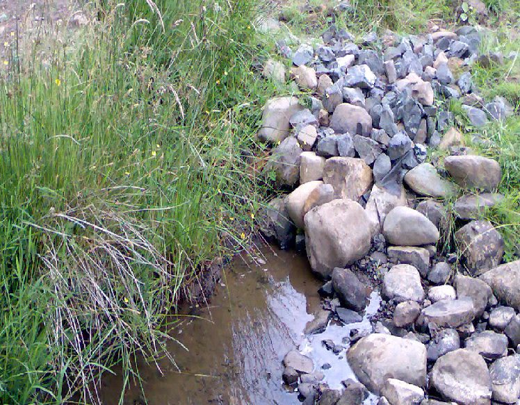 A water extraction point in a watercourse. There are a lot of river stones that can be seen from which the watercourse appears from. The abstraction point is below the river stones.