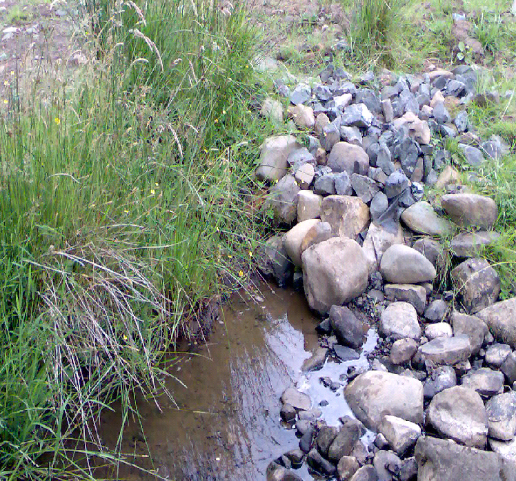 A water extraction point in a watercourse. There are a lot of river stones that can be seen from which the watercourse appears from. The abstraction point is below the river stones.