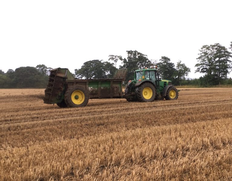 Muck spreader in action being driven by a John Deere in a stubble field