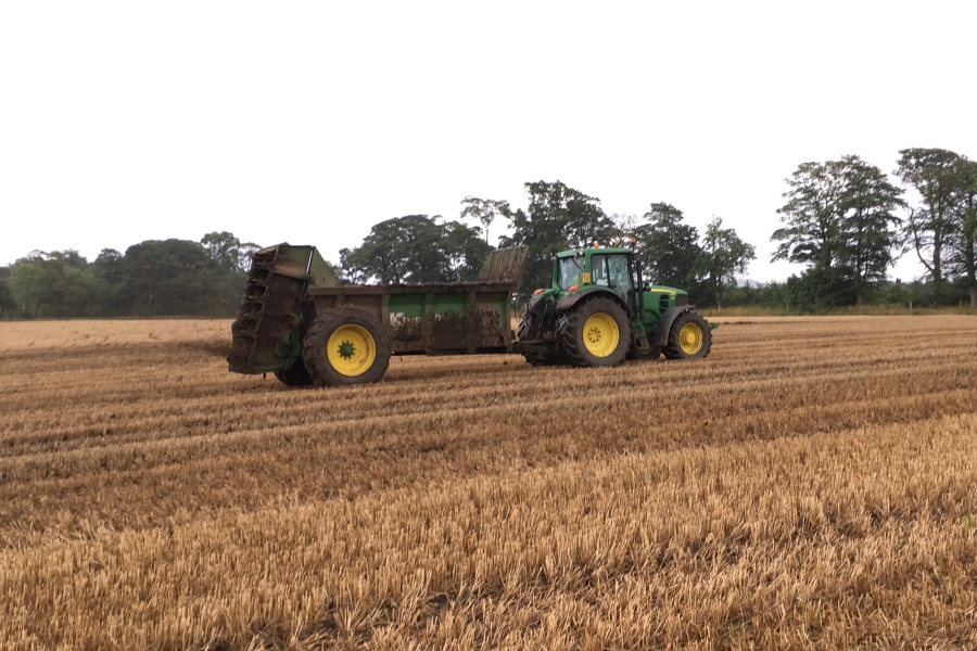 Muck spreader in action being driven by a John Deere in a stubble field