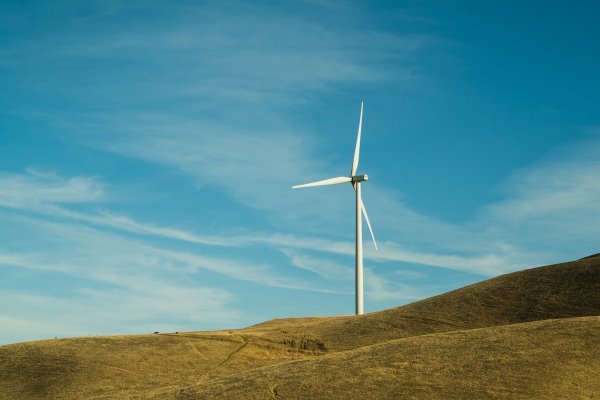 Single wind turbine on a green hill with blue sky and wispy clouds in the background