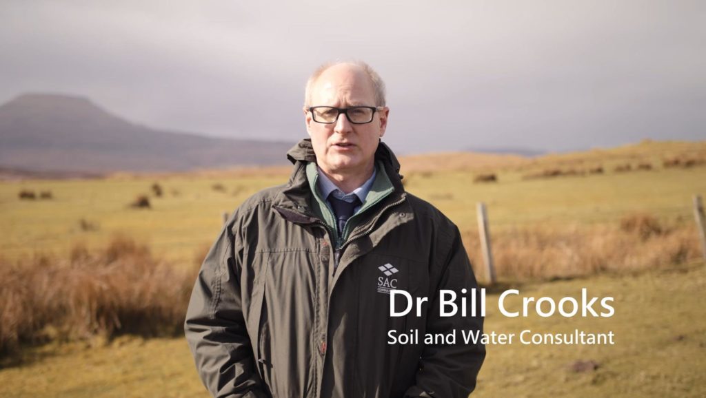 Dr Bill Crooks standing in an upland grass field with rushes prevalent in the background.