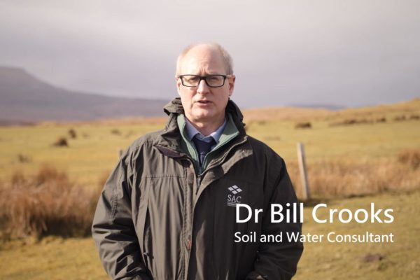 Dr Bill Crooks standing in an upland grass field with rushes prevalent in the background.