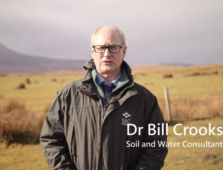 Dr Bill Crooks standing in an upland grass field with rushes prevalent in the background.