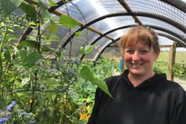 Female crofter stands in polycrub filled with plants