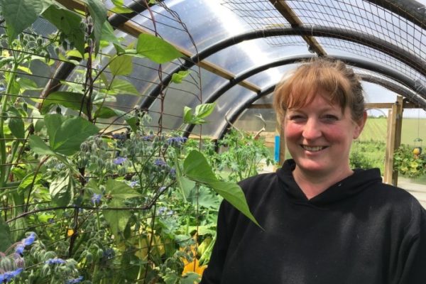 Female crofter stands in polycrub filled with plants