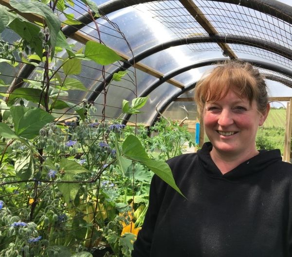 Female crofter stands in polycrub filled with plants