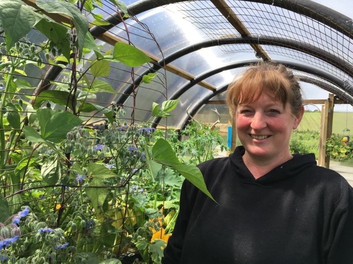 Female crofter stands in polycrub filled with plants