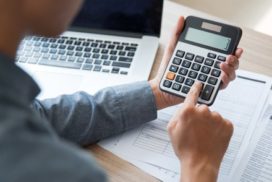 Man using calculator with laptop in background