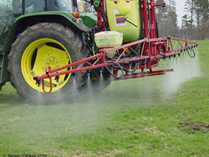 Rear mounted pesticide sprayer on a John Deere tractor and in action, spraying pesticide on a grassland field.