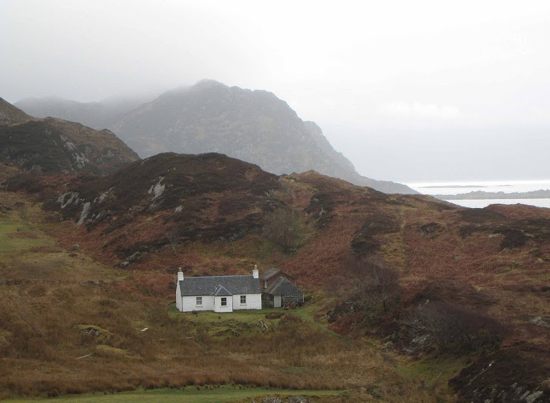 Cottage with hills and mountains in the background - lots of rushes growing on the croft