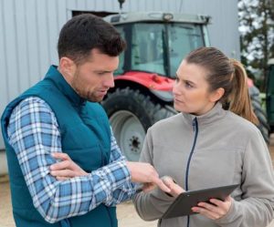 Two farmers discussing list on clipboard, tractor in background