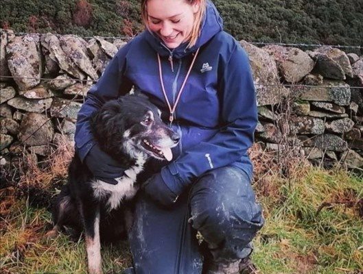 Young woman smailing and crouching down by her working dog