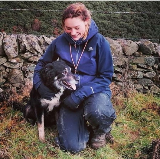 Young woman smailing and crouching down by her working dog