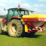 Red tractor with fertiliser spreader in green field