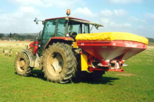 Red tractor with fertiliser spreader in green field