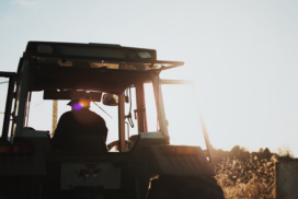 A silhouette of a man in a tractor, with the sun setting behind