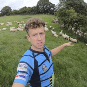 Young Farmer in a field of sheep, pointing at the sheep.