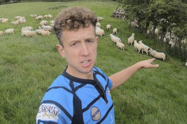 Young Farmer in a field of sheep, pointing at the sheep.