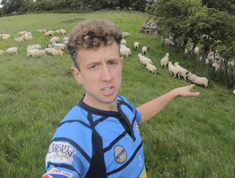 Young Farmer in a field of sheep, pointing at the sheep.