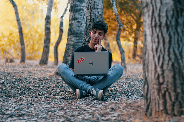 Young person sitting cross-legged on the forest floor and using a laptop