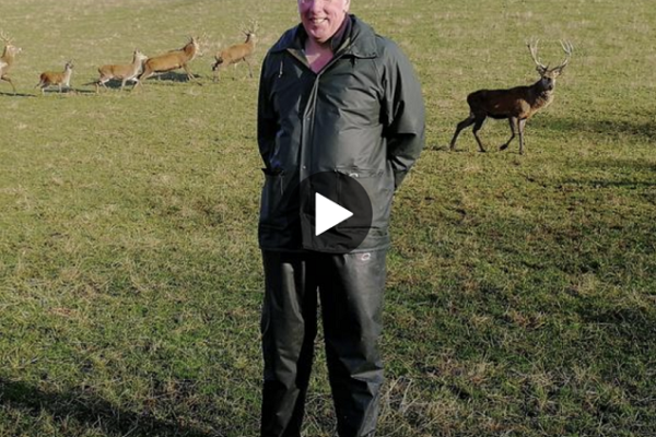 Bob Prentice stood in a field with deer behind him