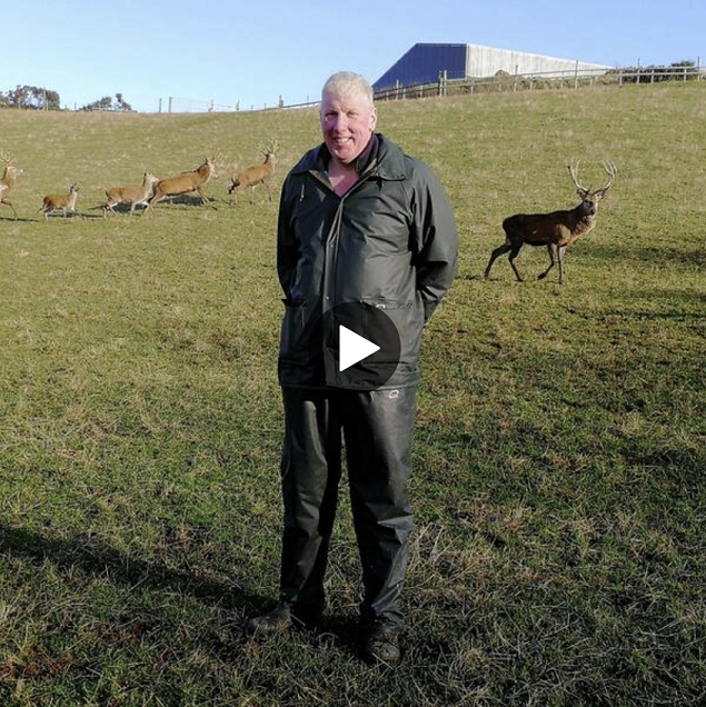 Bob Prentice stood in a field with deer behind him