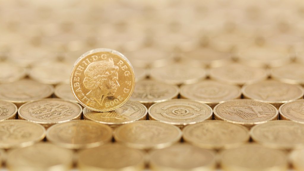 one british pound coin stood up on a surface made from other coins