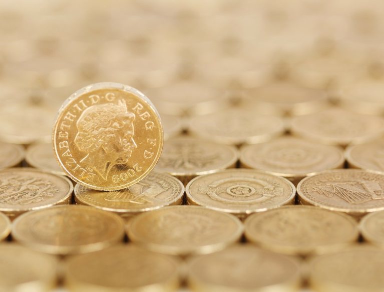 one british pound coin stood up on a surface made from other coins