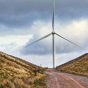 large wind turbine situated at the top of a roadway that runs between two hills.