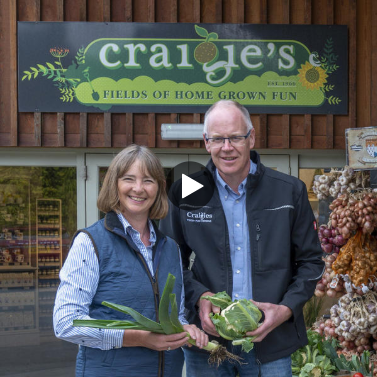 A Farming Family stood in front of their farm shop holding vegetables