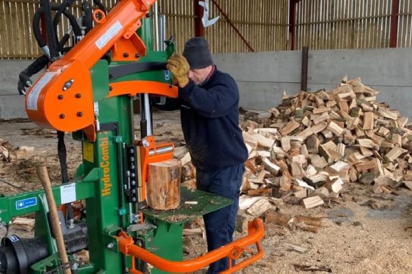 A man operating a Posch 20t Hydrocombi Firewood Log Splitter with a pile of split logs behind him