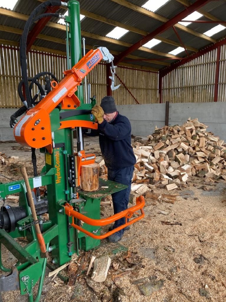 A man operating a Posch 20t Hydrocombi Firewood Log Splitter with a pile of split logs behind him