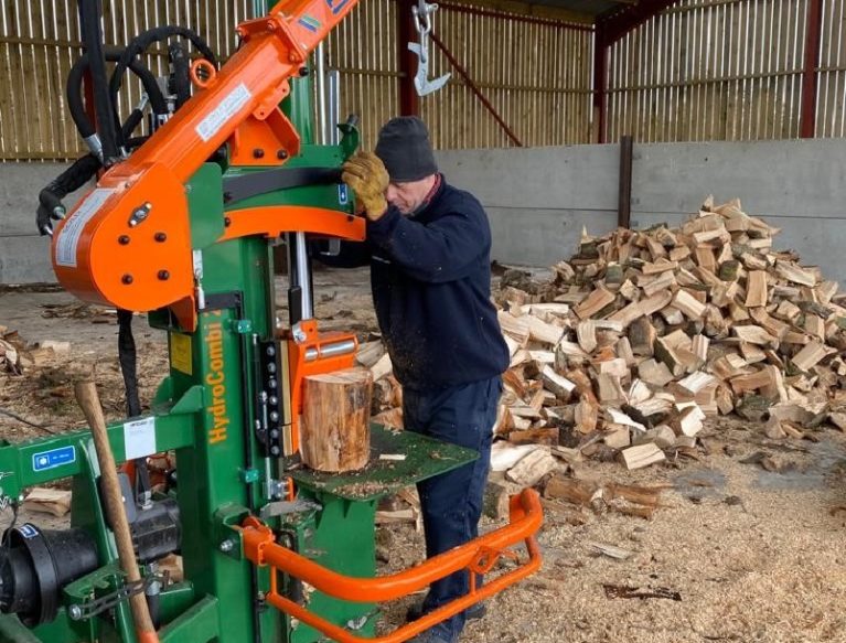 A man operating a Posch 20t Hydrocombi Firewood Log Splitter with a pile of split logs behind him