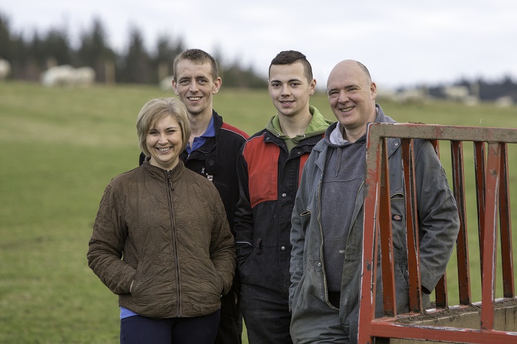 The Duffus family from Mains of Auchrianchan standing together in front of a sheep silage trailer in a grassland field.