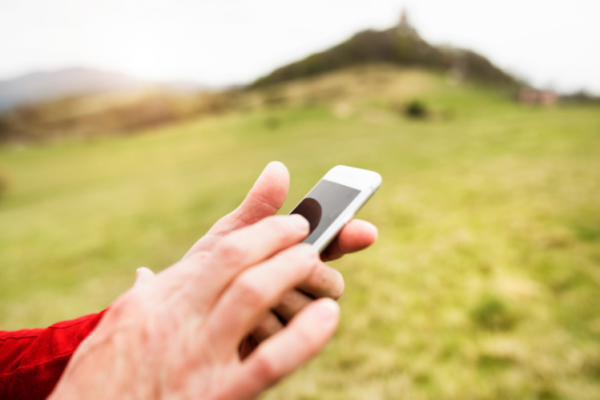 Hands tapping on a mobile phone whilst outdoors in a countryside setting.