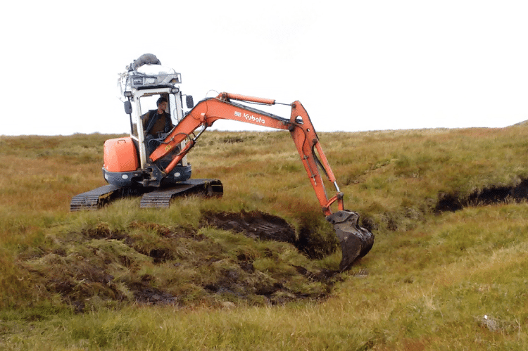 An orange digger in a moorland re-profiling a peat hagg.