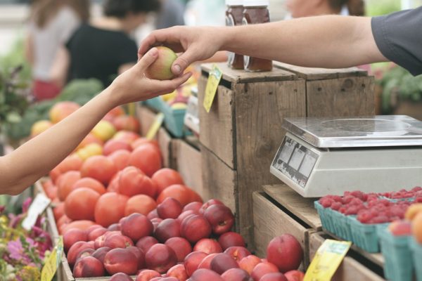 Person handing an apple to another at at fruit market