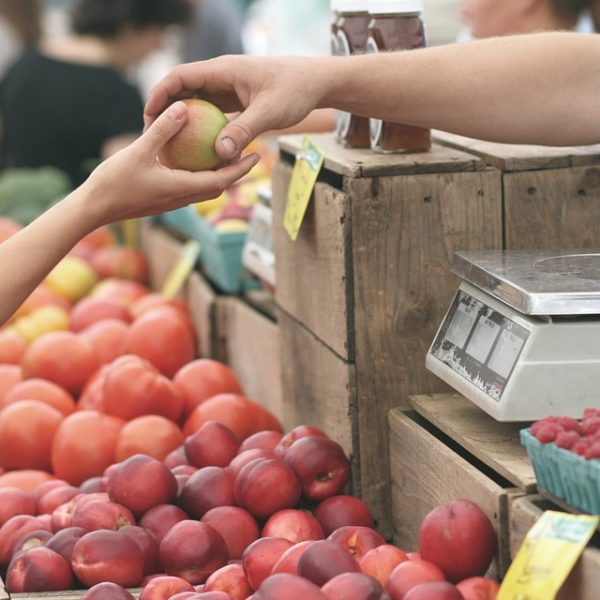 Person handing an apple to another at at fruit market
