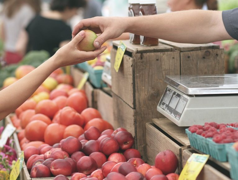 Person handing an apple to another at at fruit market