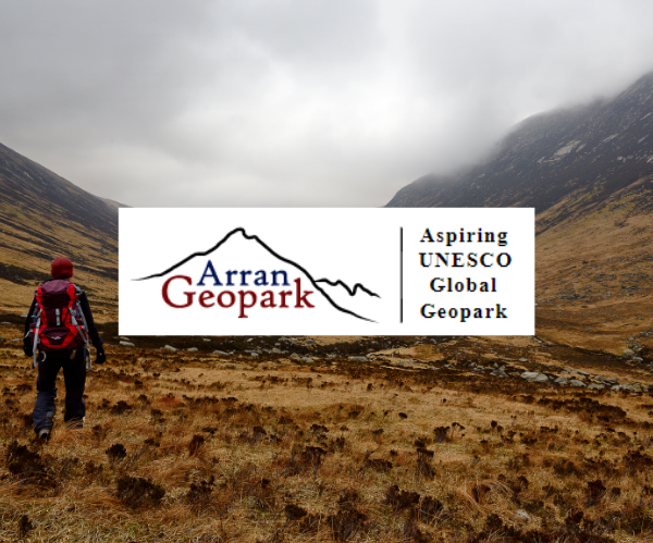 A hiker walking at the bottom of a valley on the Isle of Arran. The photo has been overlaid with the Arran Geopark logo which depicts a pencil outline of a mountain.